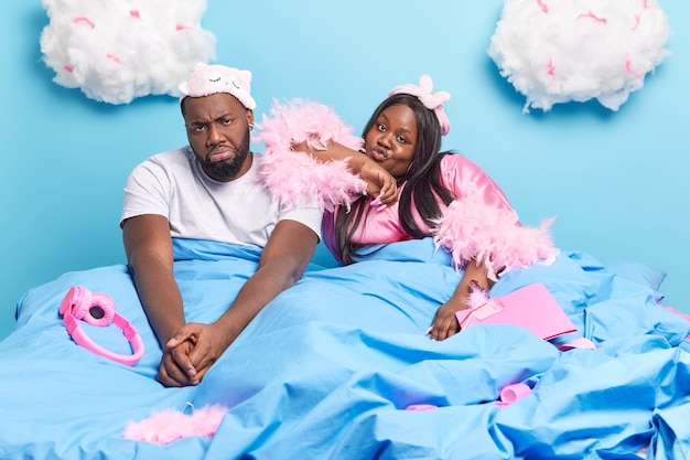 Triste ennuyé malheureux couple afro-américain rester dans un lit confortable passer le week-end à la maison habillé avec désinvolture isolé sur bleu
