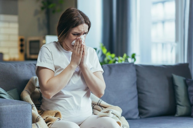 Triste femme enceinte à la maison assise sur le canapé et pleurant a le nez qui coule et les allergies éternuent dans une serviette