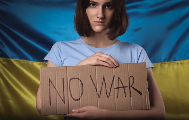 Triste femme tenant une affiche avec des mots Pas de guerre près du drapeau ukrainien
