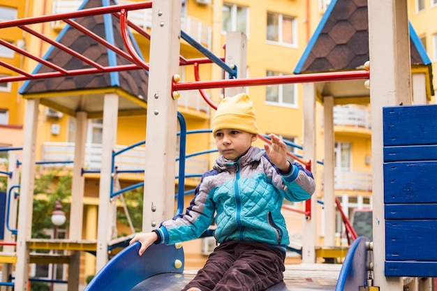 Triste garçon assis sur le toboggan jumbo et jouer seul à l'aire de jeux à l'extérieur par temps froid