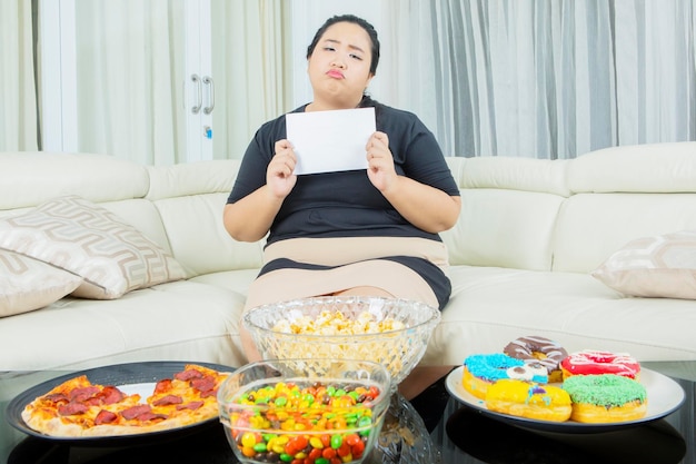 Triste grosse femme tenant un papier vierge près de la malbouffe