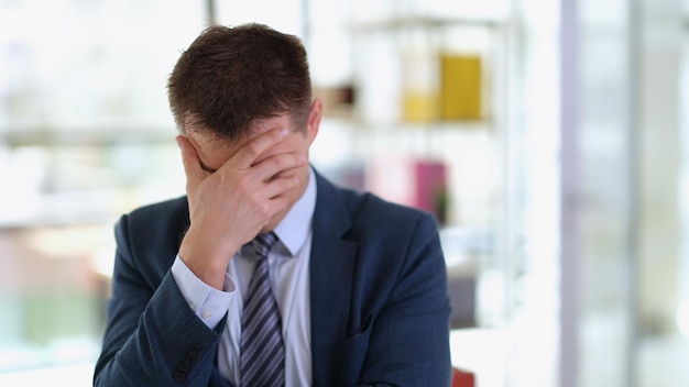 Triste homme d'affaires en costume couvrant le visage avec sa main au bureau