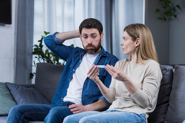 Triste homme et femme assis sur le canapé déçus par un test de grossesse négatif