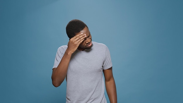 Triste homme inquiet aux prises avec des maux de tête douloureux en studio, se sentant mal et épuisé. Personne stressée dans la douleur, ayant un problème de maladie et se frottant les tempes pour soigner une migraine grave.