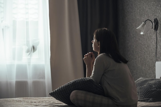 Triste jeune femme atteinte de troubles affectifs saisonniers, la dépression est assise sur le lit devant la fenêtre