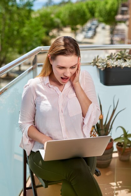 Triste jeune femme belle à l'aide d'un ordinateur portable à la maison sur le balcon