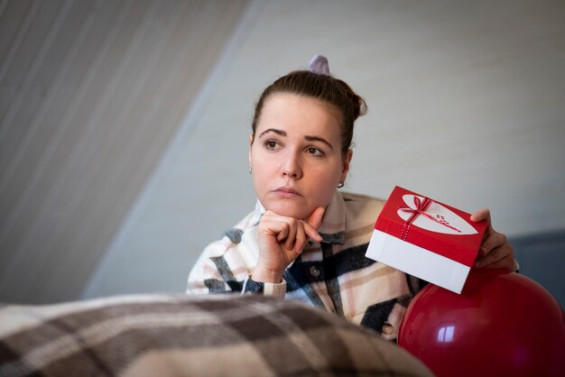 Triste jeune femme bouleversée est assise sur le lit avec boîte et ballon. Belle fille est déçue