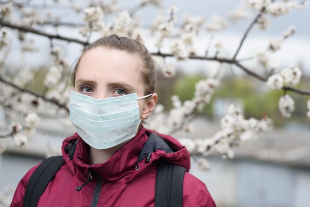 Triste jeune femme en masque de protection médical. Arbre fleurissant sur fond. Allergie de printemps.