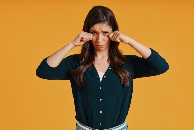 Triste jeune femme en vêtements décontractés faisant une grimace en se tenant debout sur fond jaune