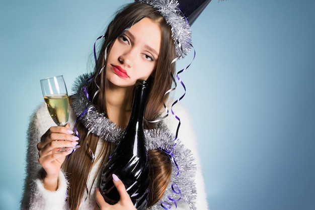 Triste jeune fille ivre dans une casquette célèbre la nouvelle année, tient du champagne dans ses mains