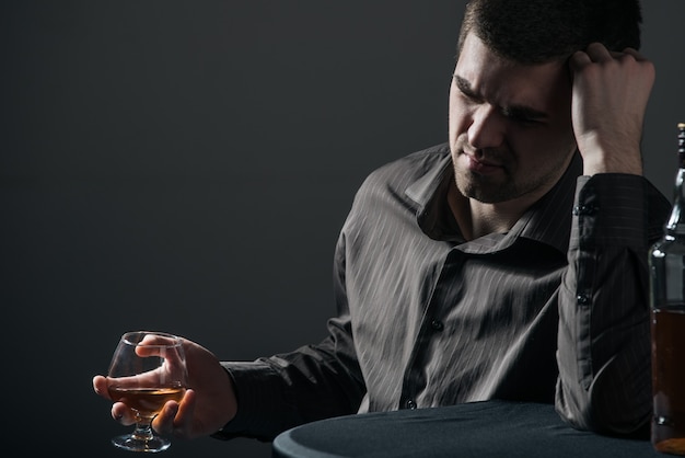 Triste jeune homme apathique boit une boisson alcoolisée sur une surface noire