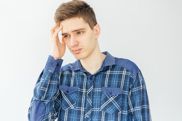 Triste jeune homme dans une chemise bleue sur fond gris clair. Dépression, problèmes et stress.