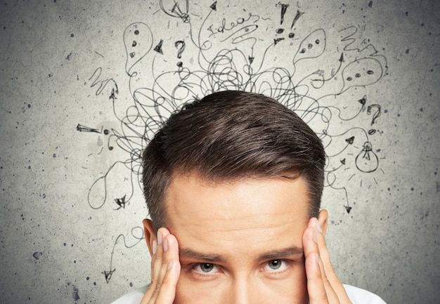 Triste jeune homme avec une expression de visage stressée et un cerveau se fondant dans des points d'interrogation de lignes.