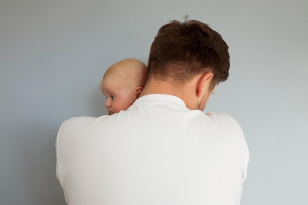 Triste jeune homme tenant un bébé de 2 mois isolé sur fond bleu