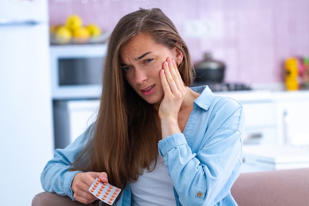 Triste malheureuse jeune femme prenant des analgésiques de maux de dents aigus à la maison. Douleur dentaire et problèmes dentaires