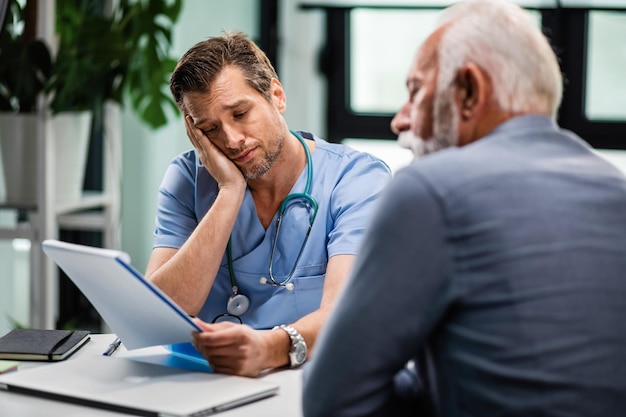 Triste médecin se sentant déçu en lisant les documents médicaux de son patient âgé lors de consultations à la clinique