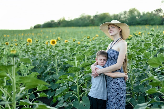 Triste petit fils embrasse une femme enceinte debout sur un champ de tournesols en fleurs