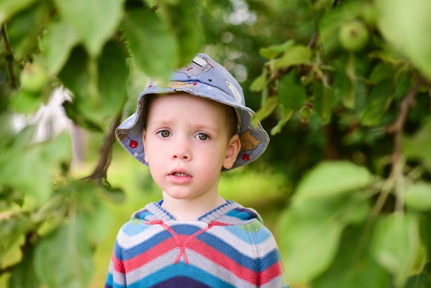 Triste petit garçon debout dans le jardin d'été