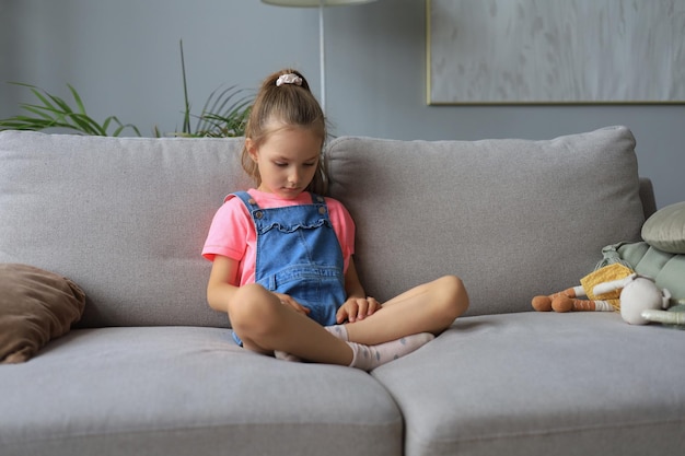 Triste petite fille assise sur un canapé seule à la maison