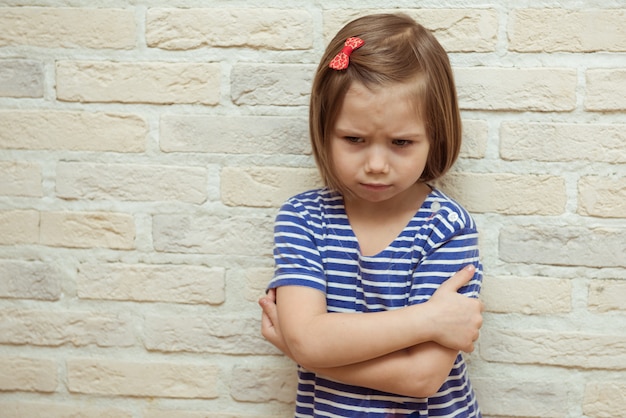 Triste petite fille contre un mur de briques.