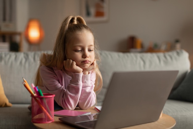 Triste petite fille utilisant un ordinateur portable ayant un épuisement professionnel assis à la maison