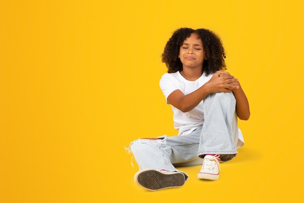 Triste pleurer adolescente afro-américaine en t-shirt blanc tenir la main sur le genou souffrant de douleur s'asseoir sur