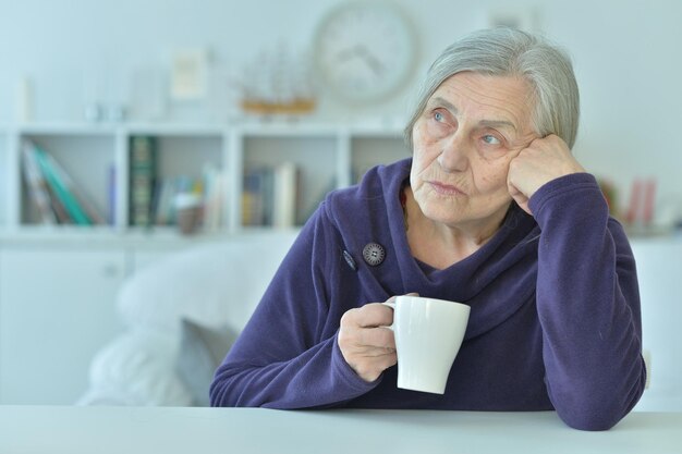 Triste vieille femme avec des maux de tête en buvant du thé