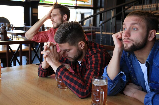 Tristes fans de football masculins regardant un match au bar et buvant de la bière.