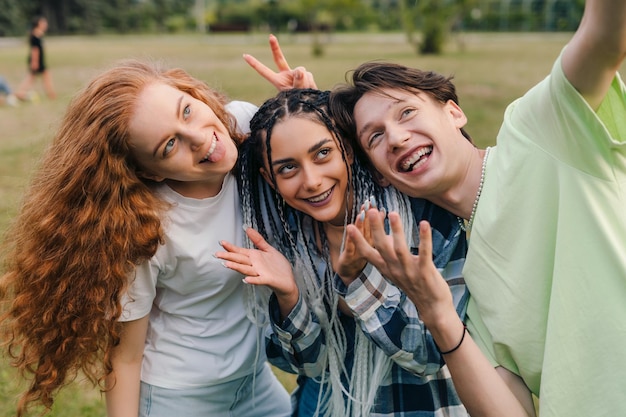 Trois adolescents prenant un selfie pour publier sur Internet debout dans le parc d'été Vloggers prenant une vidéo Trendy happy mixed people