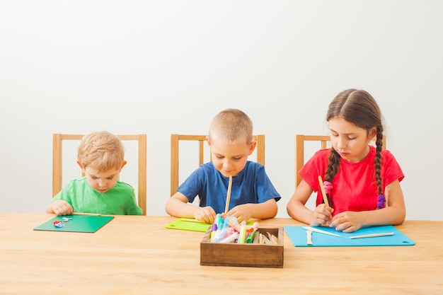 Trois adorables enfants en t-shirts colorés assis à la grande table en bois modelant avec de la pâte multicolore Atelier avec de la pâte à modeler