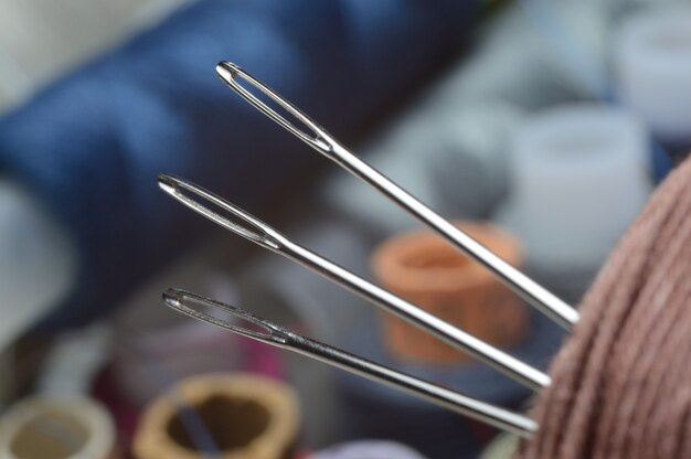 Trois aiguilles à coudre sont insérées dans une bobine de fil. fermer.