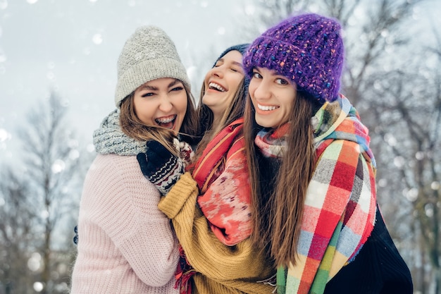 Trois amies à l'extérieur dans des chapeaux tricotés s'amusant par temps froid et neigeux