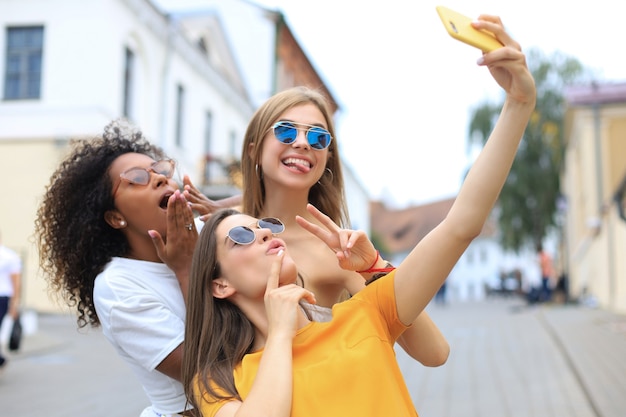 Trois amies mignonnes de jeunes filles s'amusant ensemble, prenant un selfie à la ville.