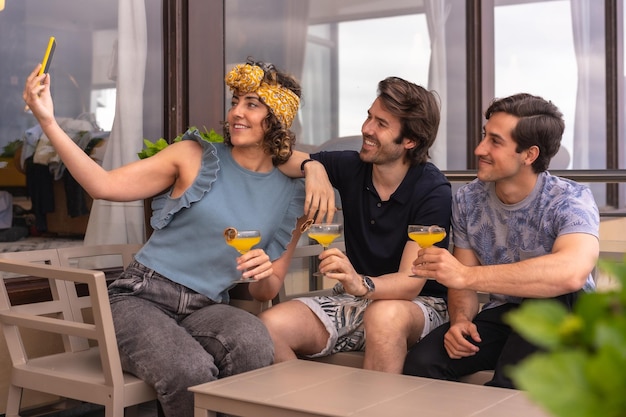 Trois amis élégants et modernes prenant un selfie pendant les vacances tout en célébrant avec des cocktails