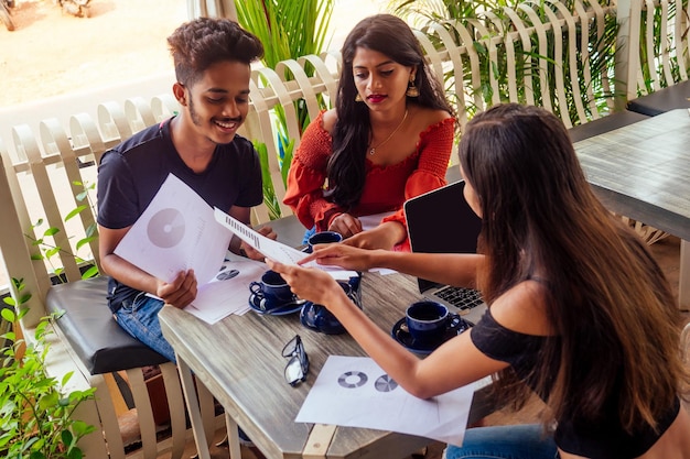 Trois amis indiens battent des crêpes sucrées avec du thé masala dans un café de plage tropicale d'été