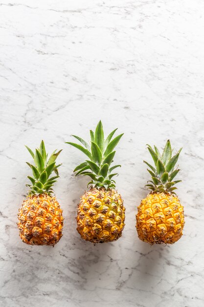 Trois ananas entiers frais avec des feuilles sur une surface en marbre.