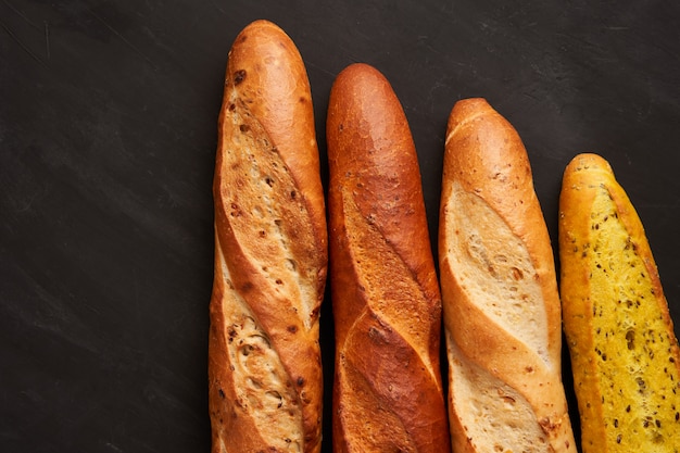 Trois baguettes françaises croustillantes se trouvent sur des graines de sésame de fond de tableau noir foncé