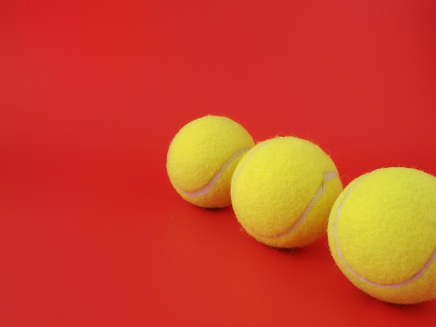 Trois balles de tennis sont alignées sur un fond rouge.