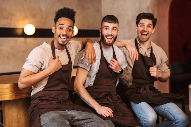 Trois baristas masculins joyeux debout au comptoir du café à l'intérieur