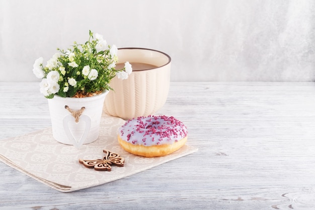 Trois beignets colorés, une tasse de café et de fleurs sur un tableau blanc