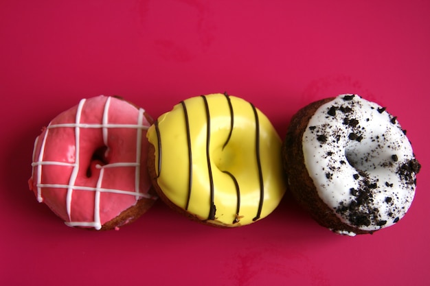 Trois beignets multicolores à peine sur fond rouge. espace de copie.