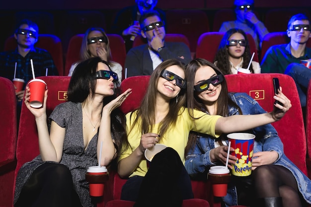 Trois belles amies riant joyeusement faisant un selfie ensemble pendant un film au cinéma