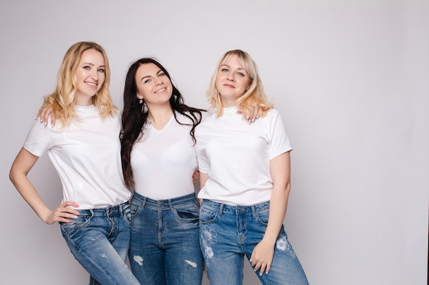 Trois belles femmes en chemises blanches et jeans posant