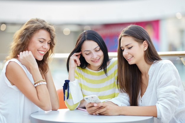 Trois belles filles élégantes sont assises à une table dans un café du centre commercial moderne et discutent après le shopping.