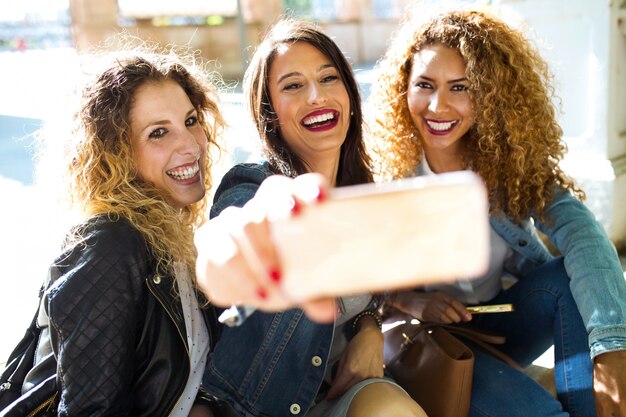 Trois belles jeunes femmes qui utilisent leur téléphone mobile dans la rue.