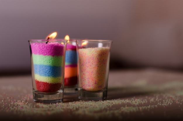 Trois bougies faites maison à partir de cire granulée colorée dans des verres.