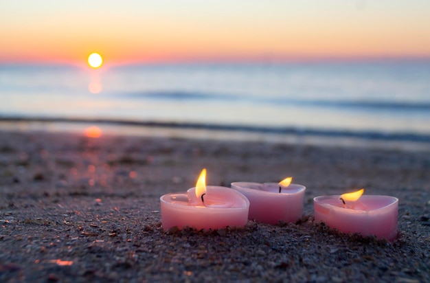 Trois bougies en forme de coeur brûlent sur le sable sur la plage de la mer près des vagues de la mer contre le backgro