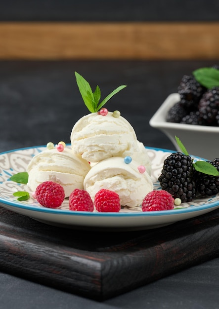 Trois boules de glace blanche dans une assiette ronde avec des feuilles de menthe sur un tableau noir