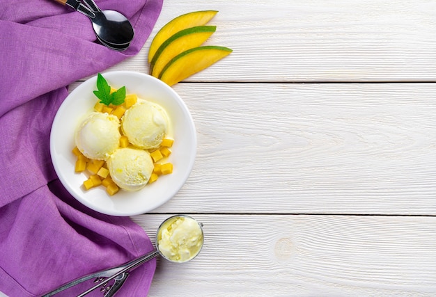 Trois boules de glace à la mangue tranches de mangue fraîche sur un mur blanc avec une serviette violette. Vue de dessus, copiez l'espace.