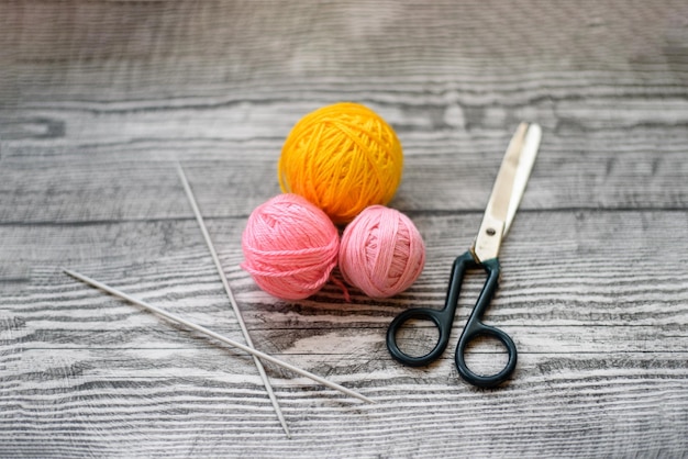 Trois boules de laine colorées aiguilles à tricoter et ciseaux sur le fond en bois